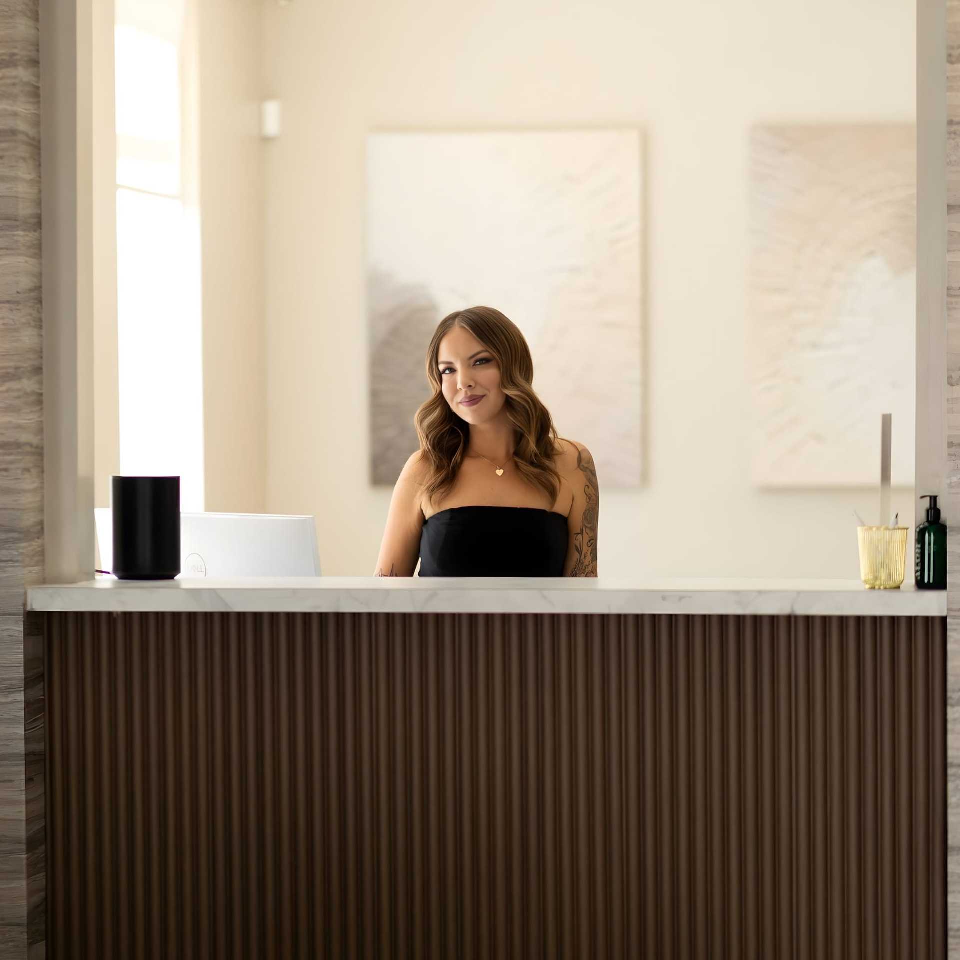 Receptionist at a modern front desk with abstract art in the background.