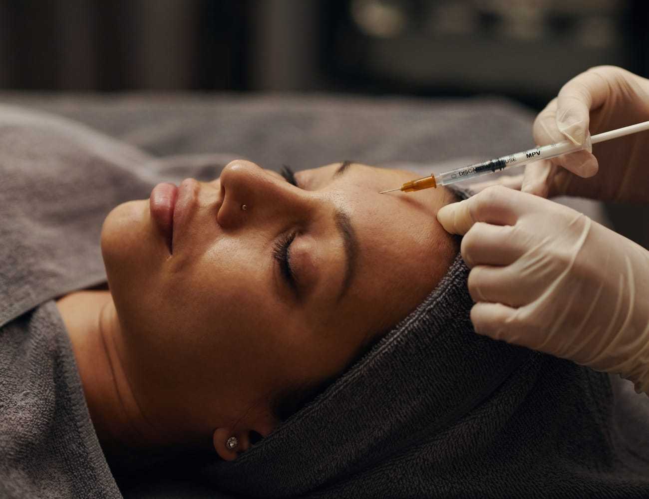 Person receiving a facial injection, lying down with a towel on the head.